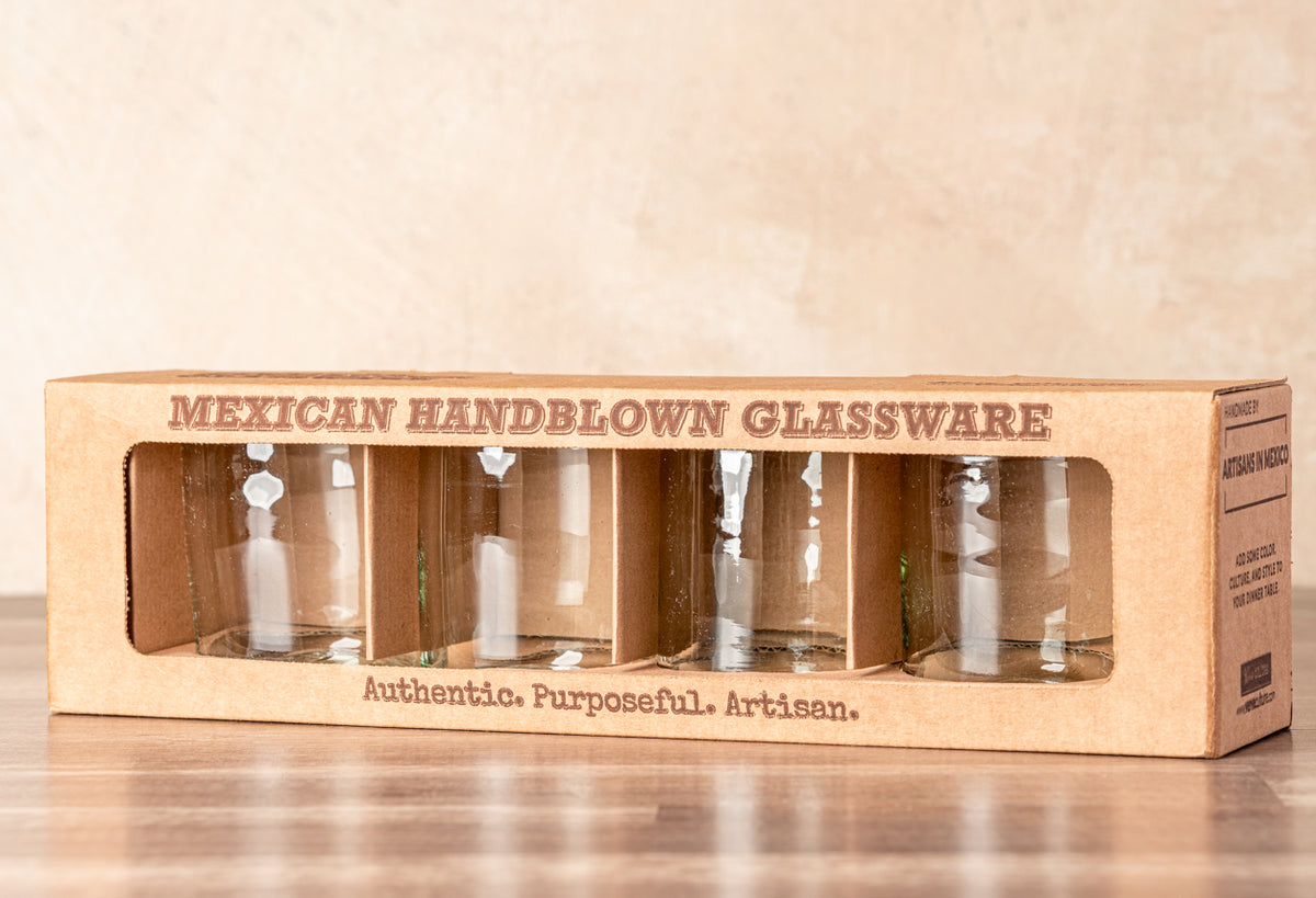 Set of four clear handblown glasses displayed in cardboard packaging with window cutout.