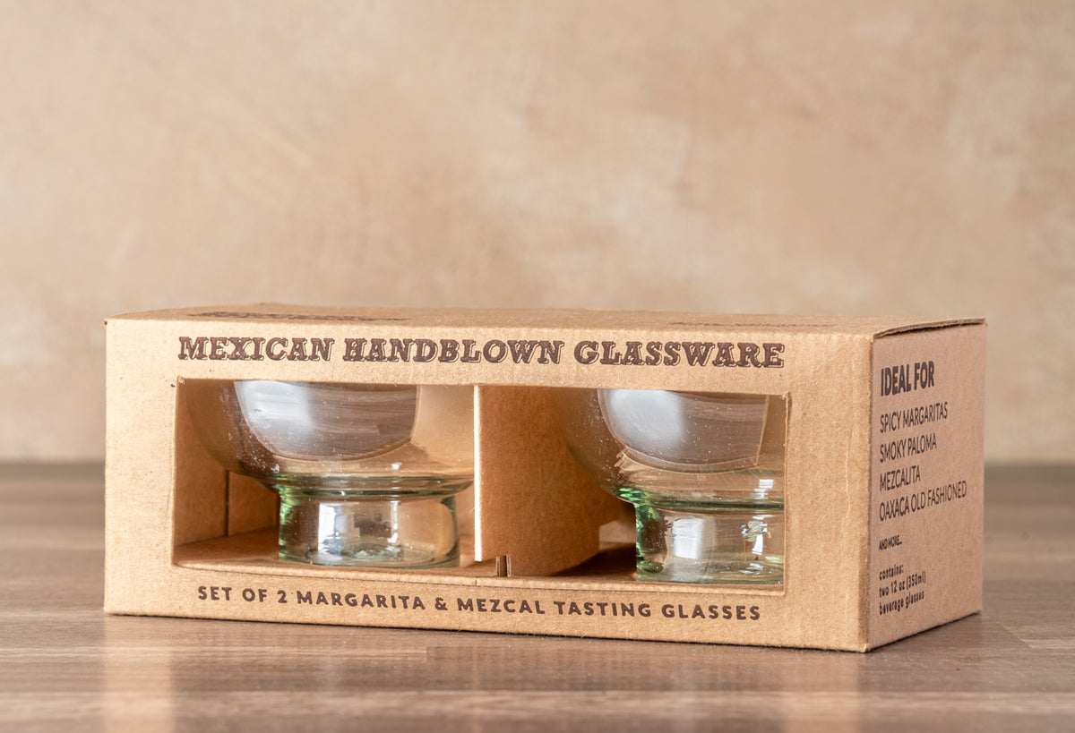 Two clear handblown glasses with green accent bands in kraft paper packaging labeled "Mexican Handblown Glassware."