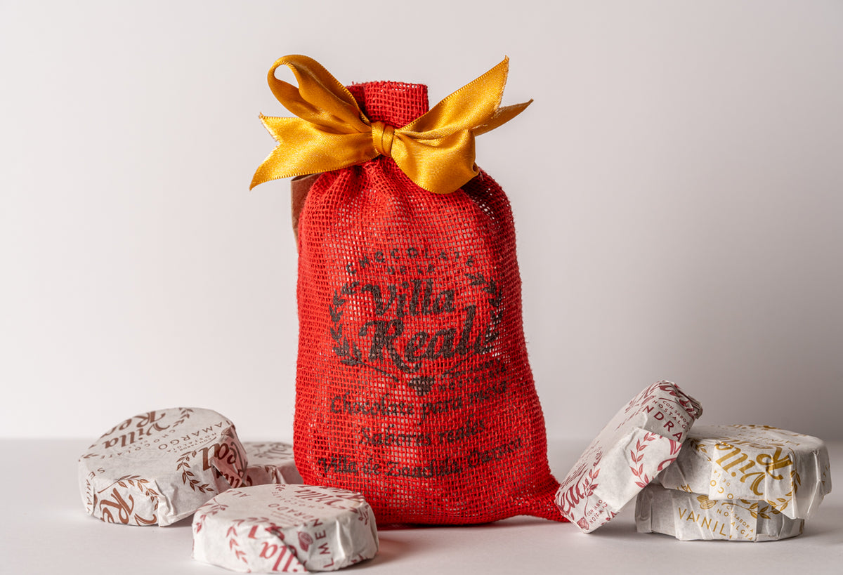 Red mesh gift bag with gold ribbon bow surrounded by four wrapped chocolate products with red and gold patterned packaging.