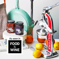 Turquoise manual citrus juicer with handle displayed next to lemons, oranges, and jam jars on white surface.