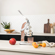 Manual citrus juicer with wood and metal construction, positioned on kitchen counter with fresh citrus fruits and glass.