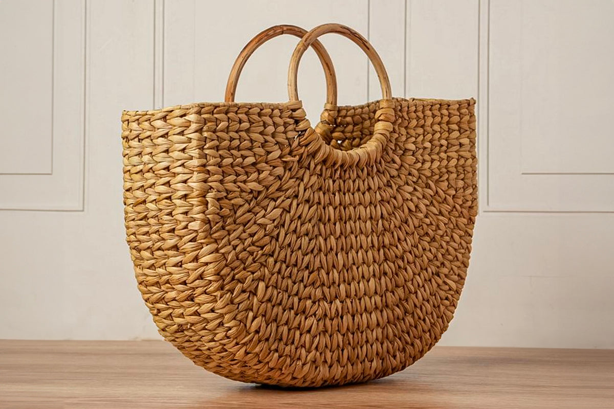 Woven straw tote bag with circular wooden handles and rounded bottom shape in natural tan color.