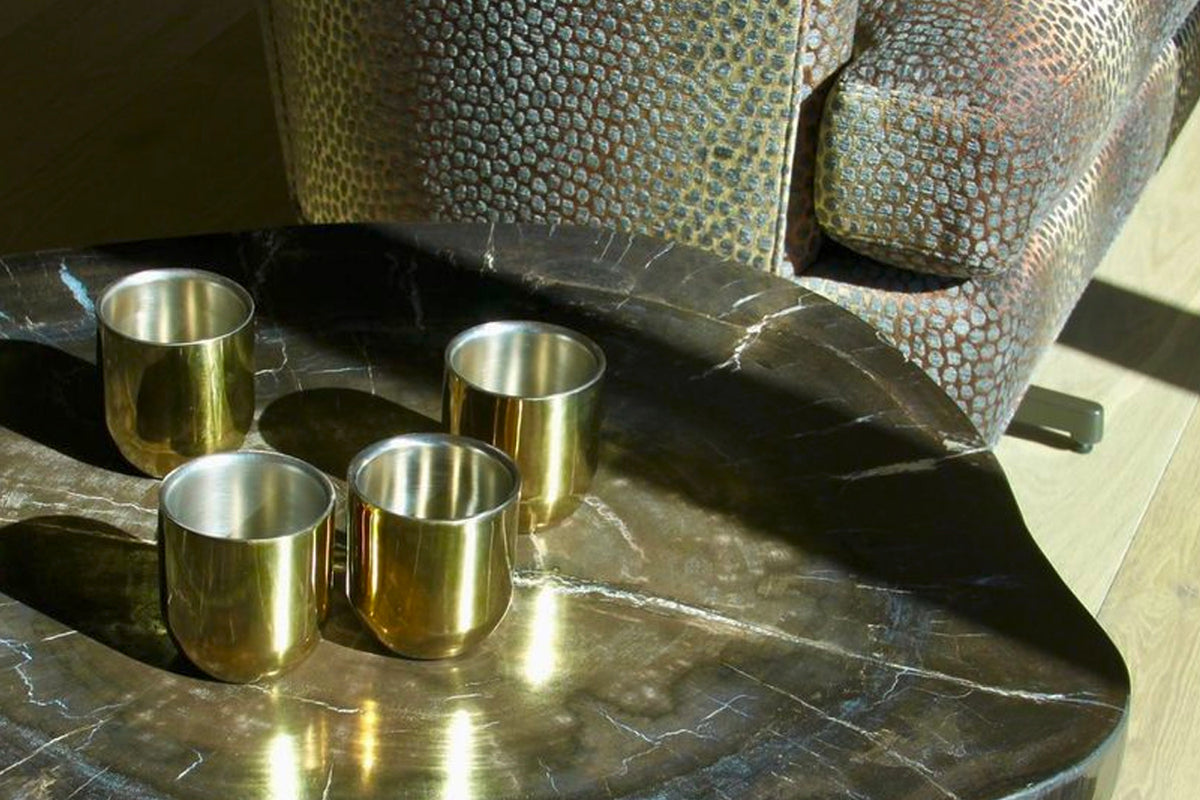 Four brass-colored double-walled cups with stainless steel interiors displayed next to patterned storage containers.