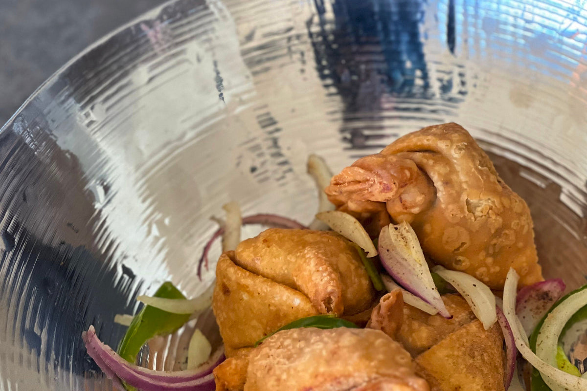 Stainless steel wok with textured surface containing fried dumplings and sliced onions and peppers.