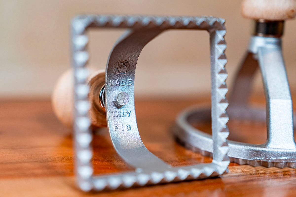 Metal ravioli stamp with square shape, decorative crimped edges, and "Made in Italy" marking on handle.