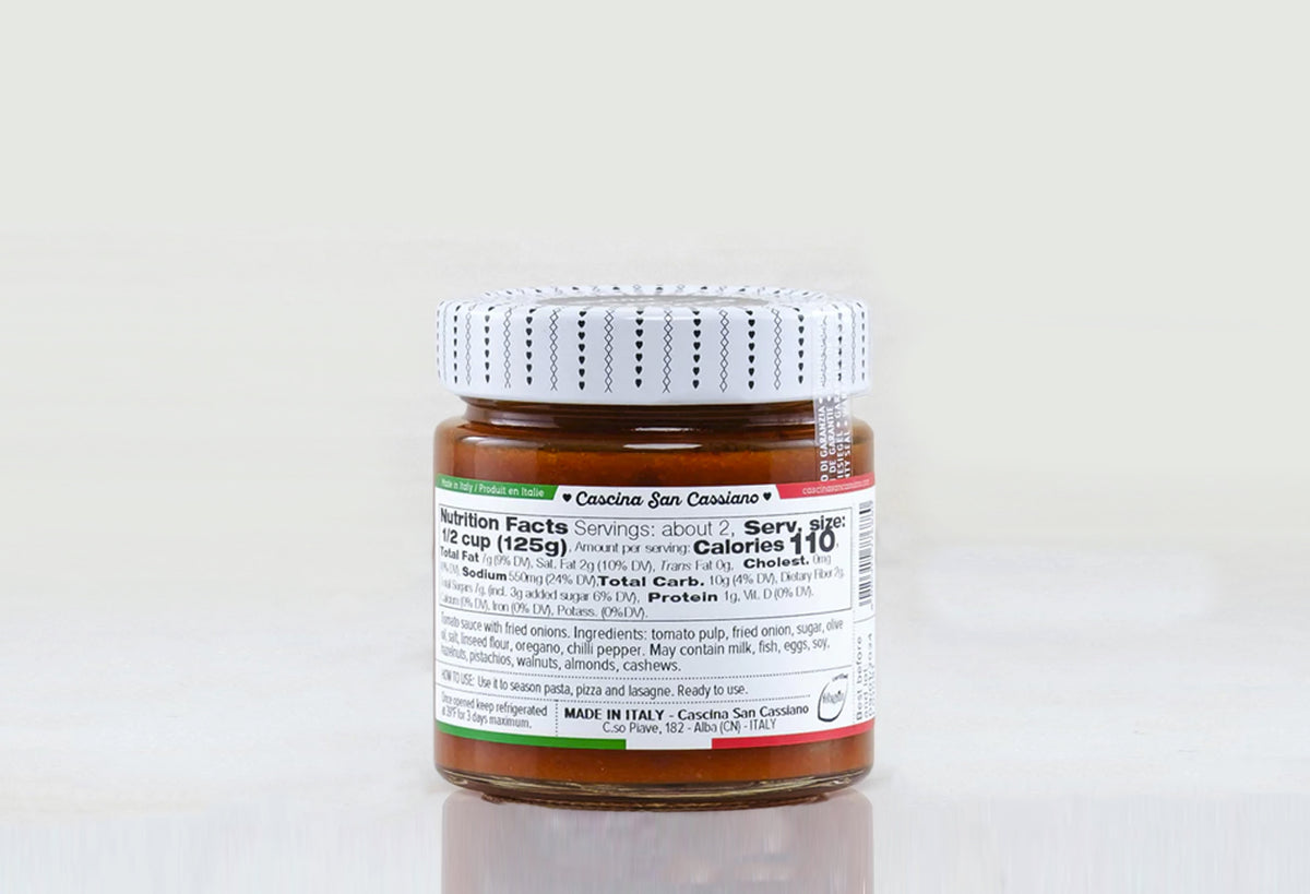 Glass jar with white dotted lid containing red-brown pizza sauce with visible fried onion pieces and nutrition label.