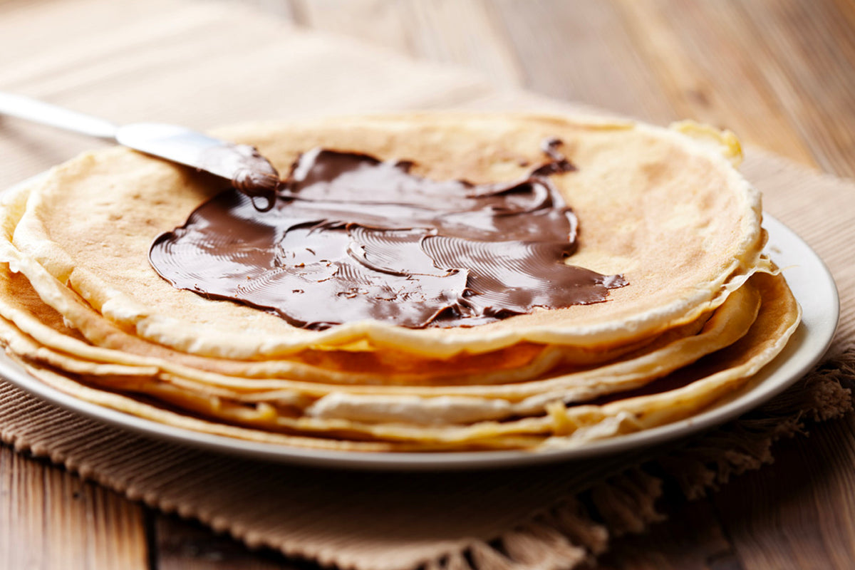 Brown hazelnut spread spread on crepes stacked on a white plate.