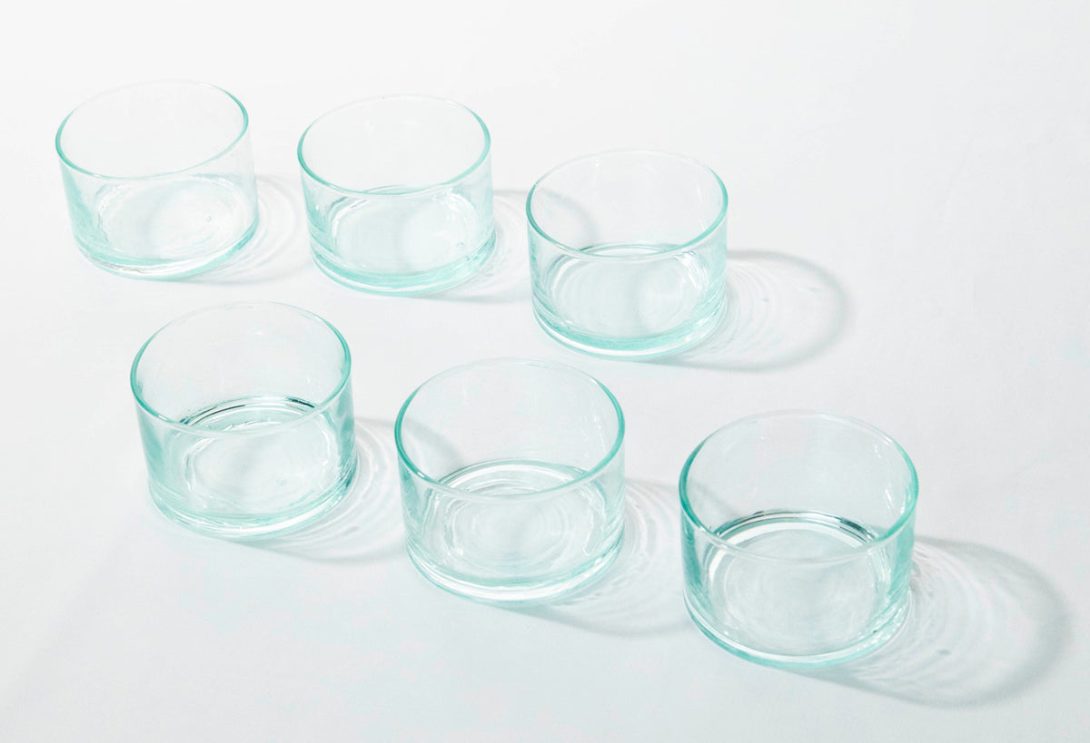 Six clear glass cups with turquoise rims arranged in two rows on a white surface.
