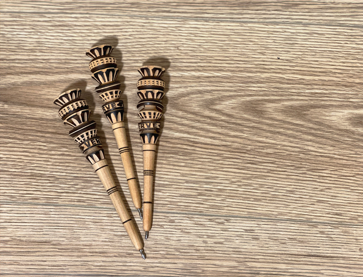 Three wooden pens with carved decorative tops featuring geometric patterns in dark and light tones.