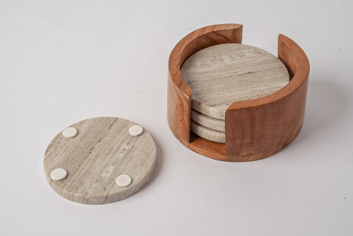 Four tan marble coasters with white feet in a wooden holder with curved handles.