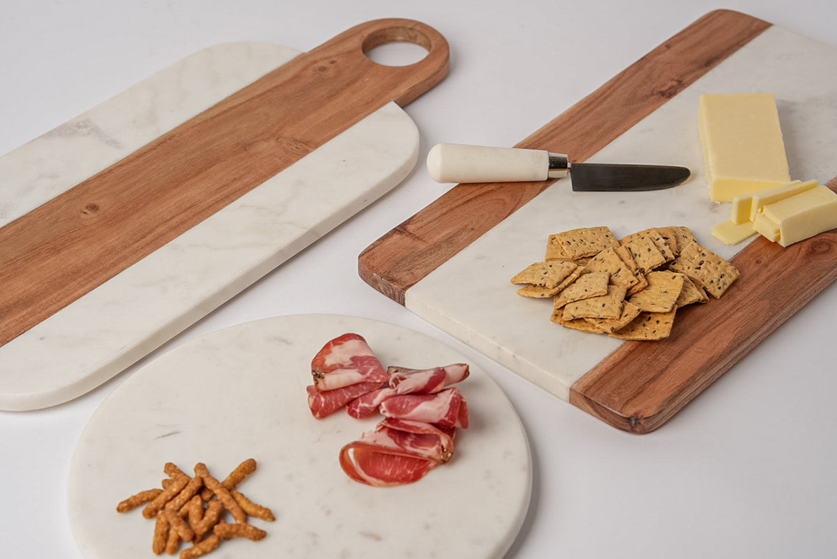 Rectangular serving boards with acacia wood and white marble sections, displayed with cheese, crackers, and cured meats.