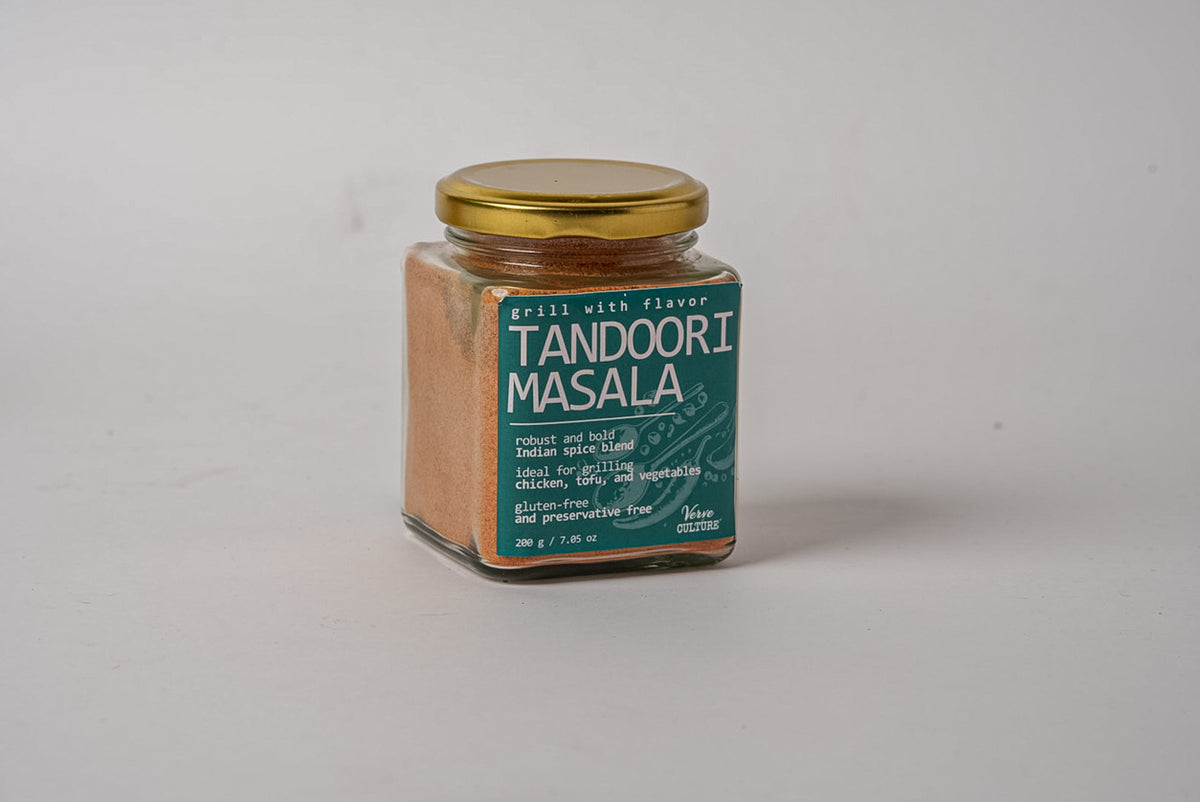 Glass jar with gold lid containing reddish-brown tandoori masala spice blend with green label.