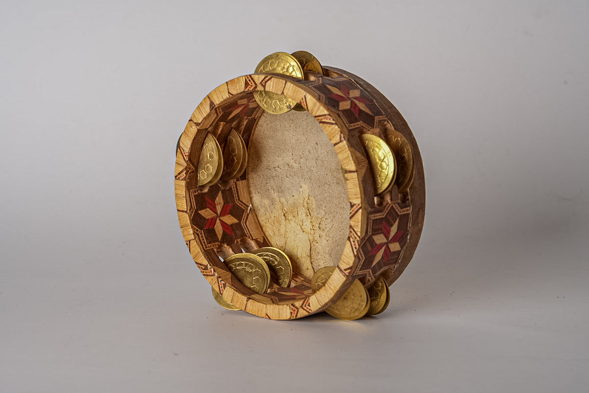 Wooden tambourine with natural parchment head, brass jingles, and geometric inlay design in brown and tan tones.
