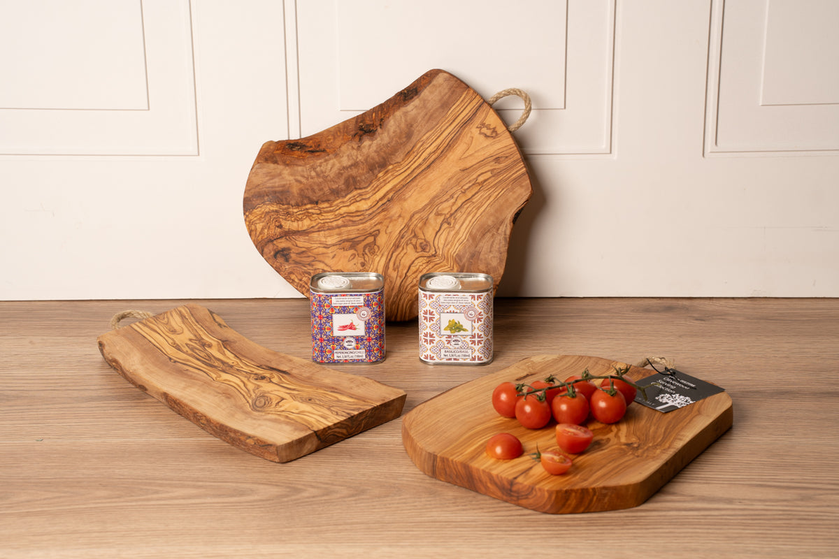 Olivewood charcuterie board with rope handle, shown with two smaller boards, jars, and tomatoes on a wooden surface.