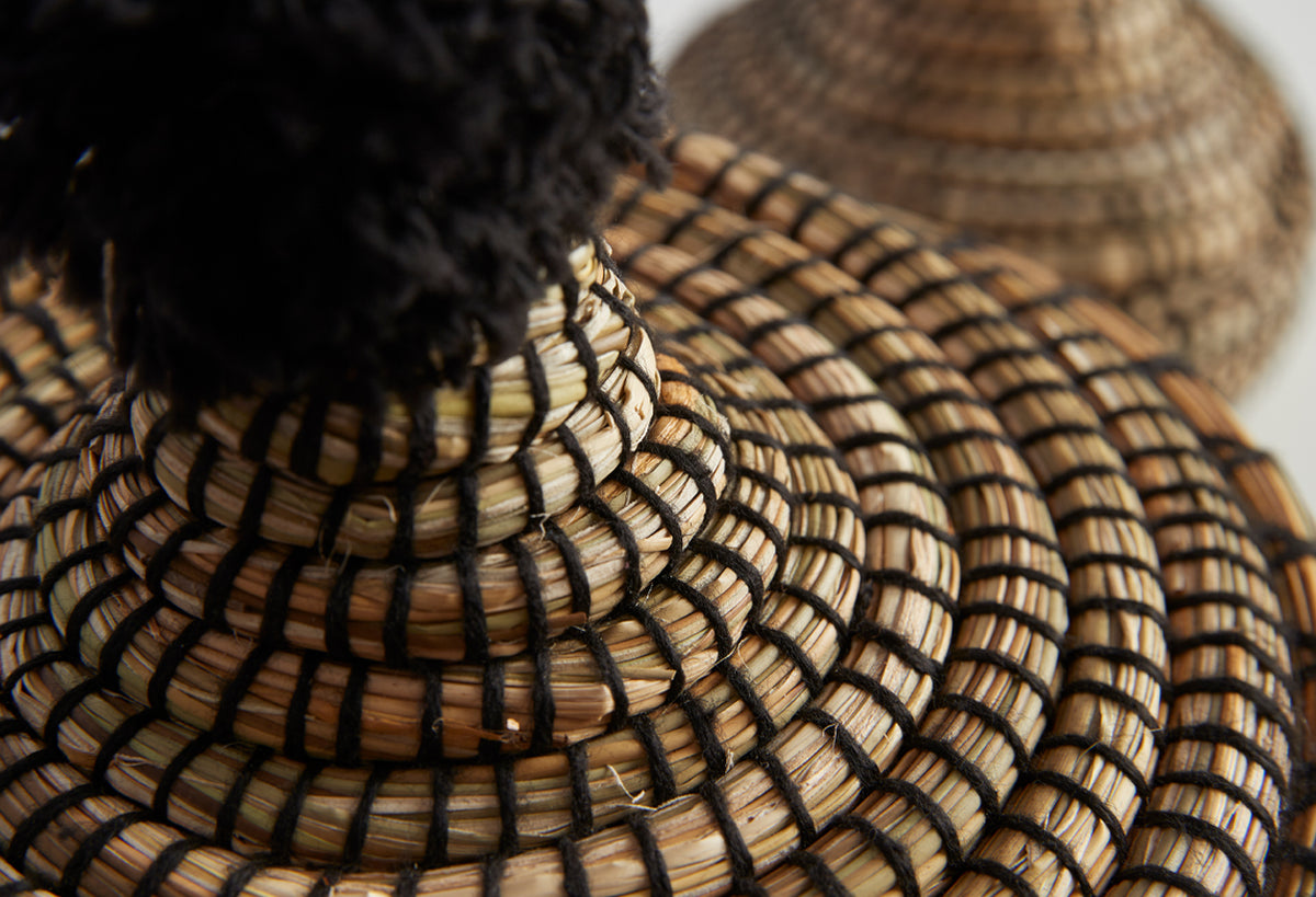 Two woven straw baskets with geometric patterns and black trim, one with a lid.