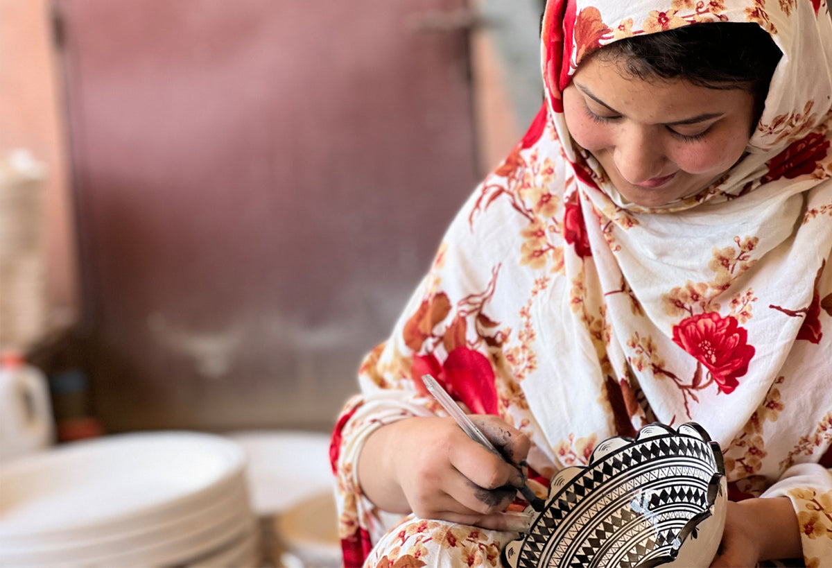 Person hand-painting geometric patterns onto a ceramic bowl in black and white design.