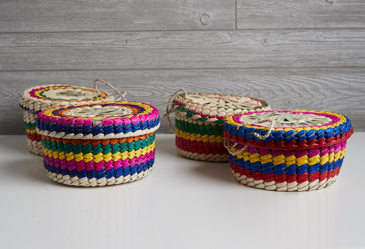 Woven palm baskets with colorful textile trim in pink, blue, yellow, and green stripes, displayed on white surface.