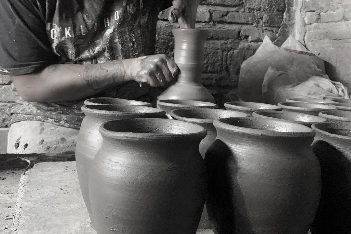 Four handmade clay cups with rounded bottoms and wide rims arranged on a work surface.