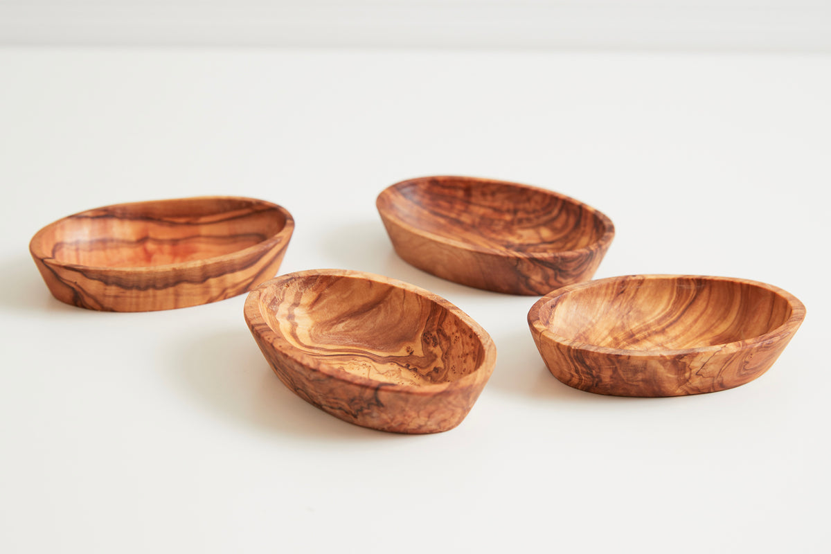 Four oval wooden bowls with natural grain patterns in medium brown tones arranged on a white surface.