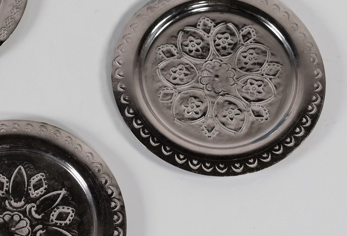 Silver coasters with embossed floral and geometric patterns arranged in circular design.