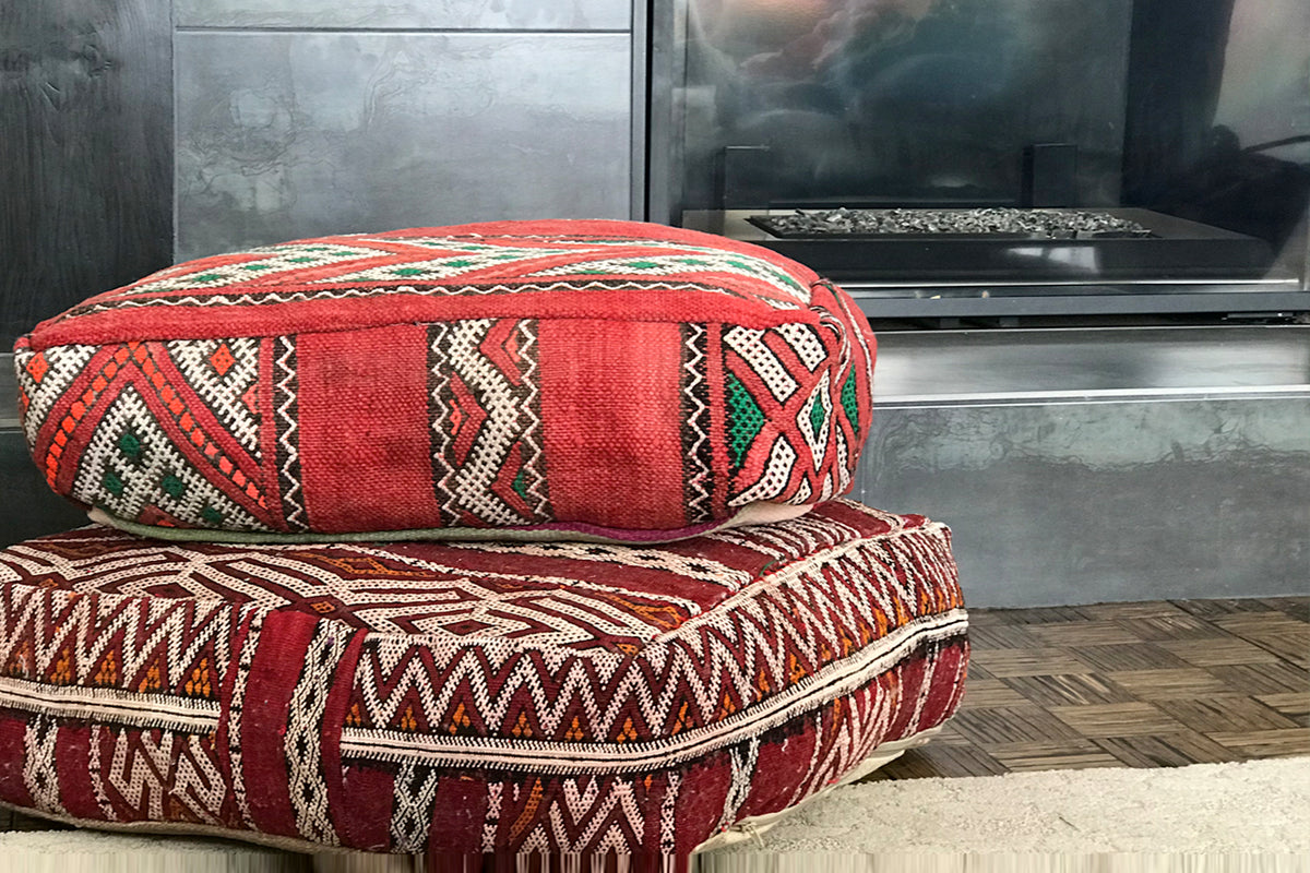 Two stacked Moroccan kilim poufs with red and cream geometric patterns in a modern interior setting.