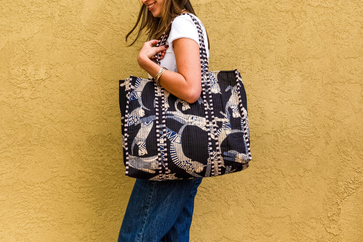 Woman holding a quilted black tote bag with white cat silhouettes and checkered pattern details.