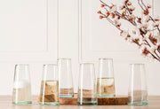 Six cone-shaped champagne glasses with colored glass bases, some filled with champagne or sparkling wine.