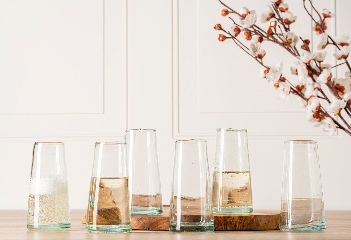 Six cone-shaped champagne glasses with colored glass bases, some filled with champagne or sparkling wine.