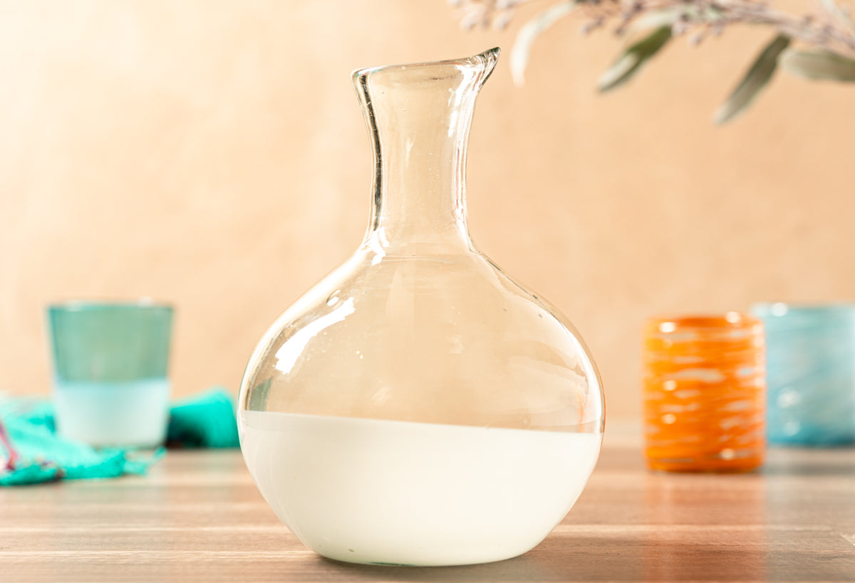 Clear glass carafe with wide rounded base and narrow neck, partially filled with white liquid.