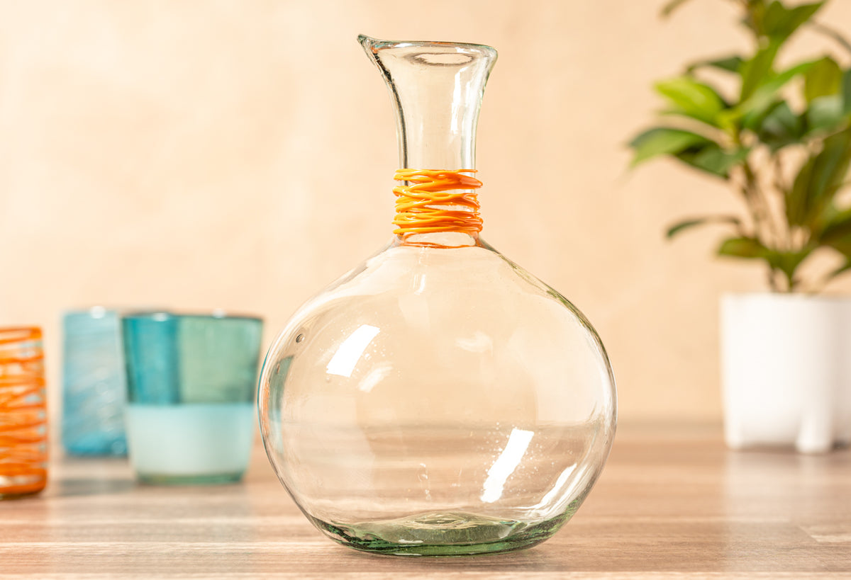 Clear glass carafe with orange-wrapped neck and tapered pouring spout, displayed on wooden surface.
