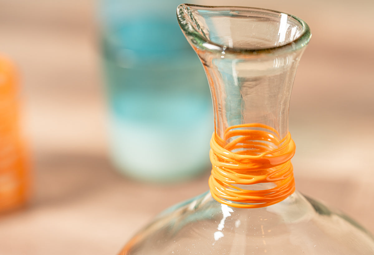 Clear glass carafe with orange wrapped neck detail and flared rim.
