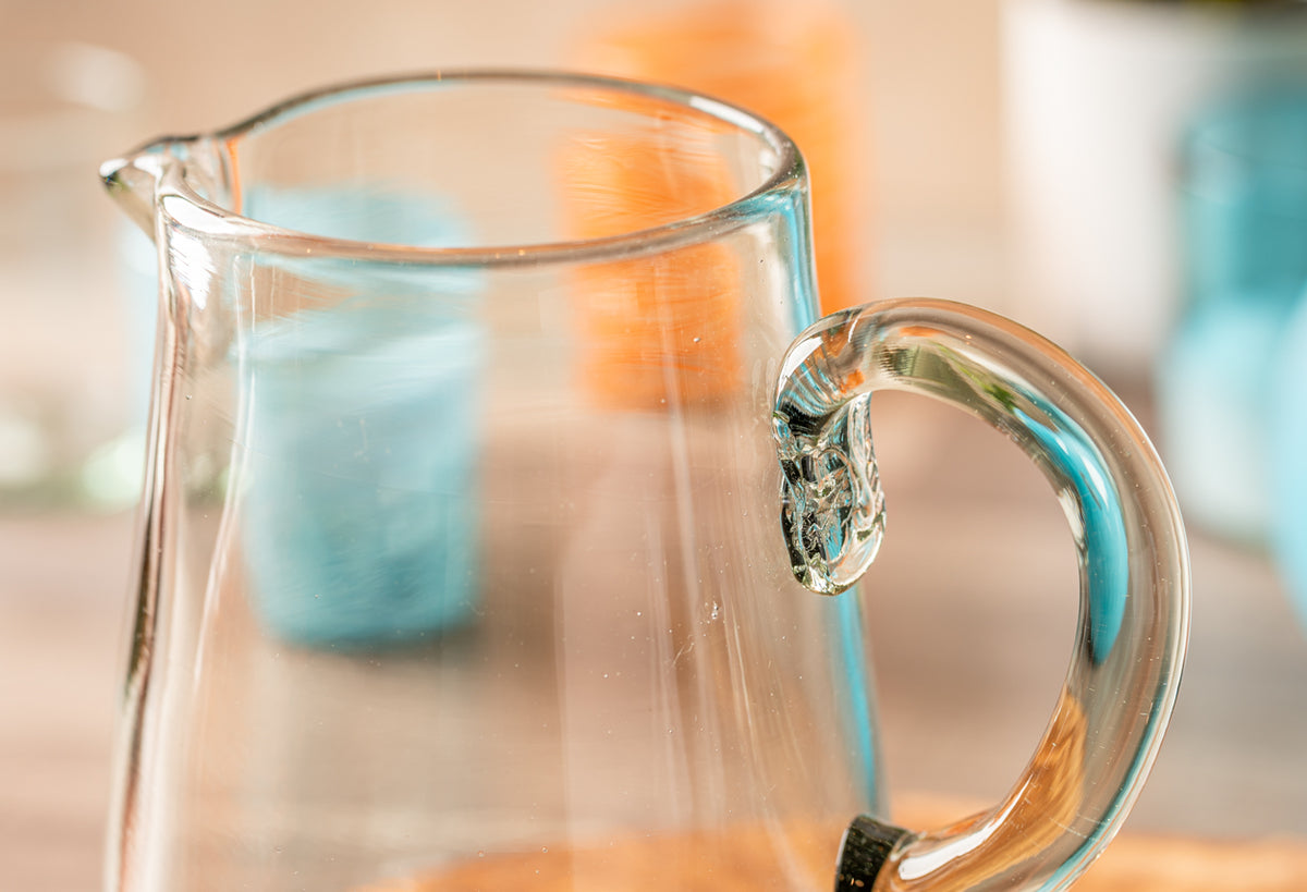 Clear glass pitcher with applied handle and pouring spout, shown from front angle.