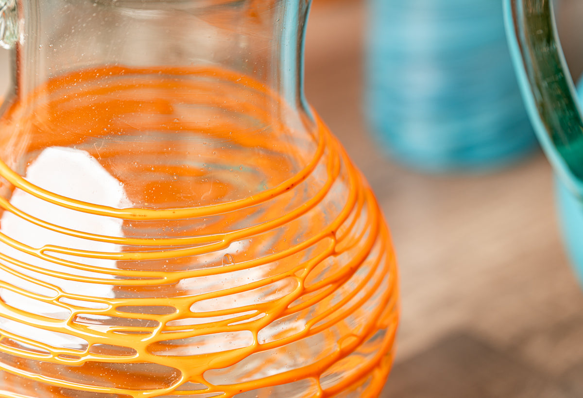 Clear glass pitcher with orange and yellow wavy stripe pattern throughout the body.