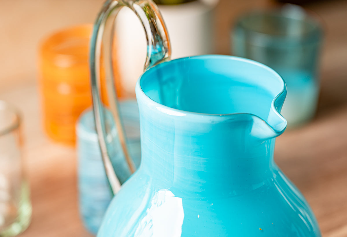 Clear glass pitcher with turquoise blue interior and white rim, featuring a curved spout for pouring.