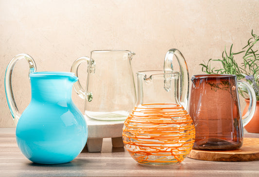 Four glass pitchers in varying sizes and colors: turquoise, clear, orange with textured wrap, and amber.