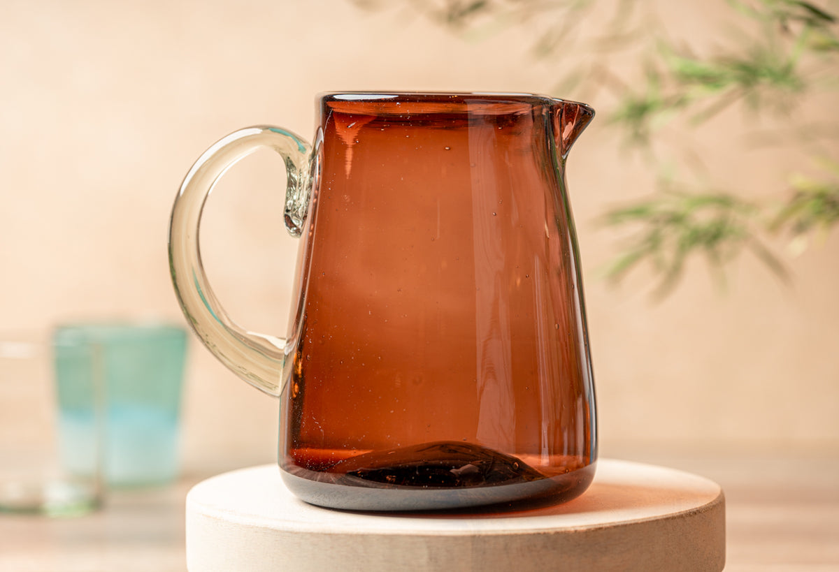 Amber glass pitcher with clear handle and pouring spout on wooden surface.