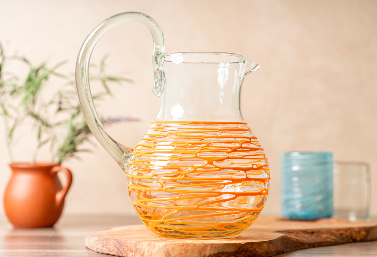 Clear glass pitcher with orange wrapped design and curved handle.