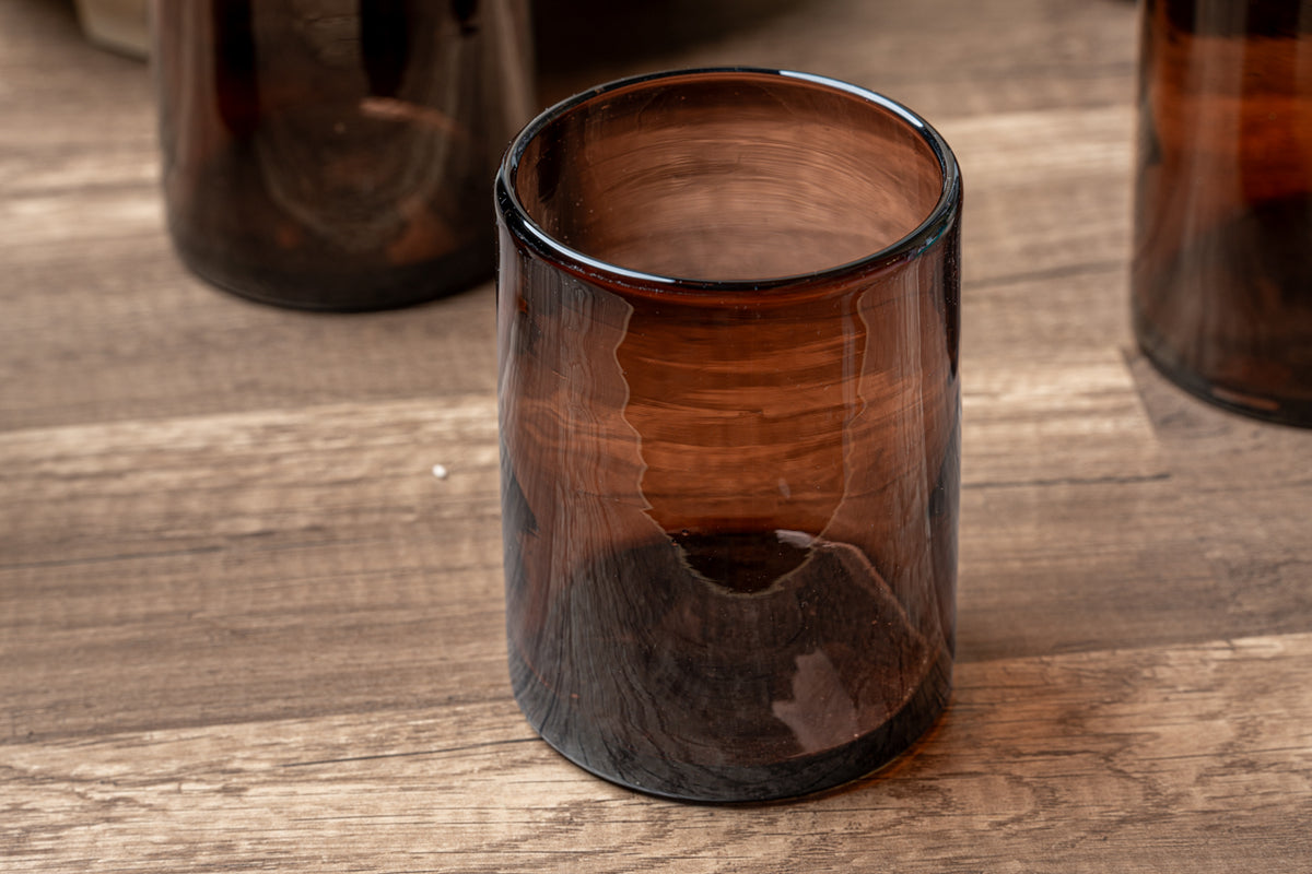 Four tamarind-colored handblown glass cups with irregular surfaces and dark brown tones on wooden surface.
