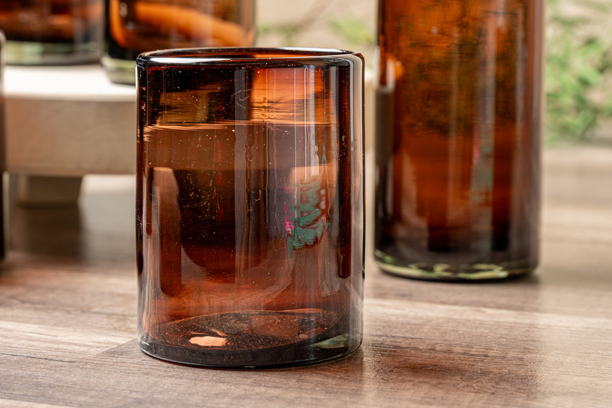Four tamarind-colored handblown glasses with dark amber glass, displayed filled with liquid on a wooden surface.