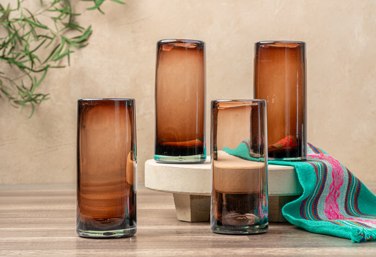 Four tamarind-colored handblown glasses with varying heights and dark gradient bases, displayed with decorative cloth.