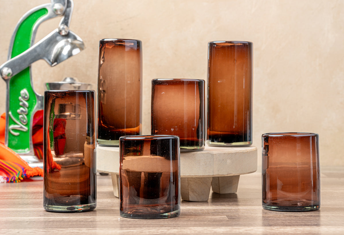 Four handblown glasses in tamarind brown with varying heights, displayed on a white ceramic base.