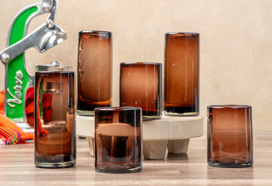 Four handblown glasses in tamarind brown with varying heights, displayed on a white ceramic base.