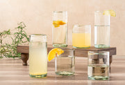 Set of six clear handblown glasses in various sizes filled with water and beverages, garnished with lemon slices.