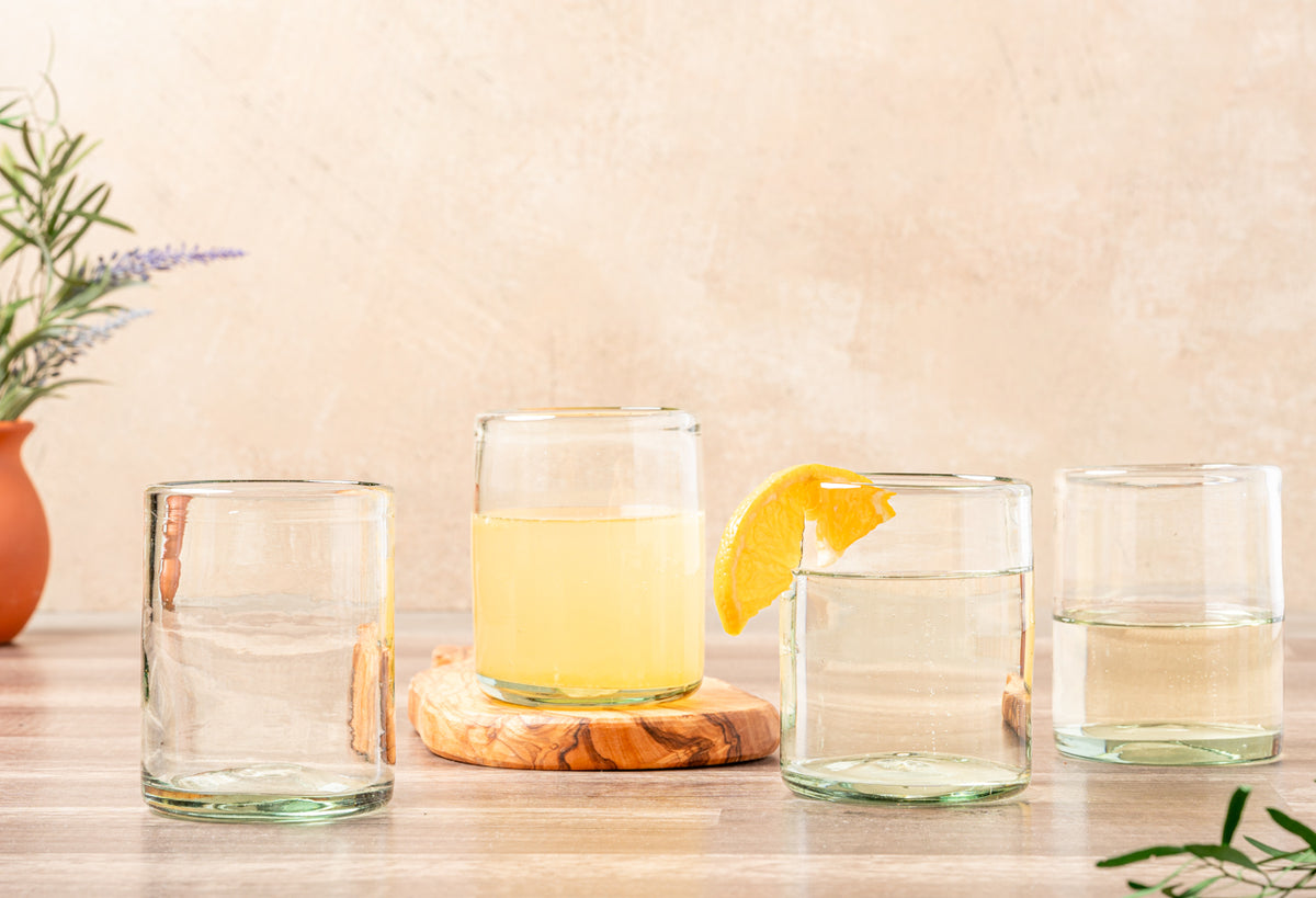 Four clear handblown glasses with gold rims, containing water and yellow liquid, one with lemon slice garnish.