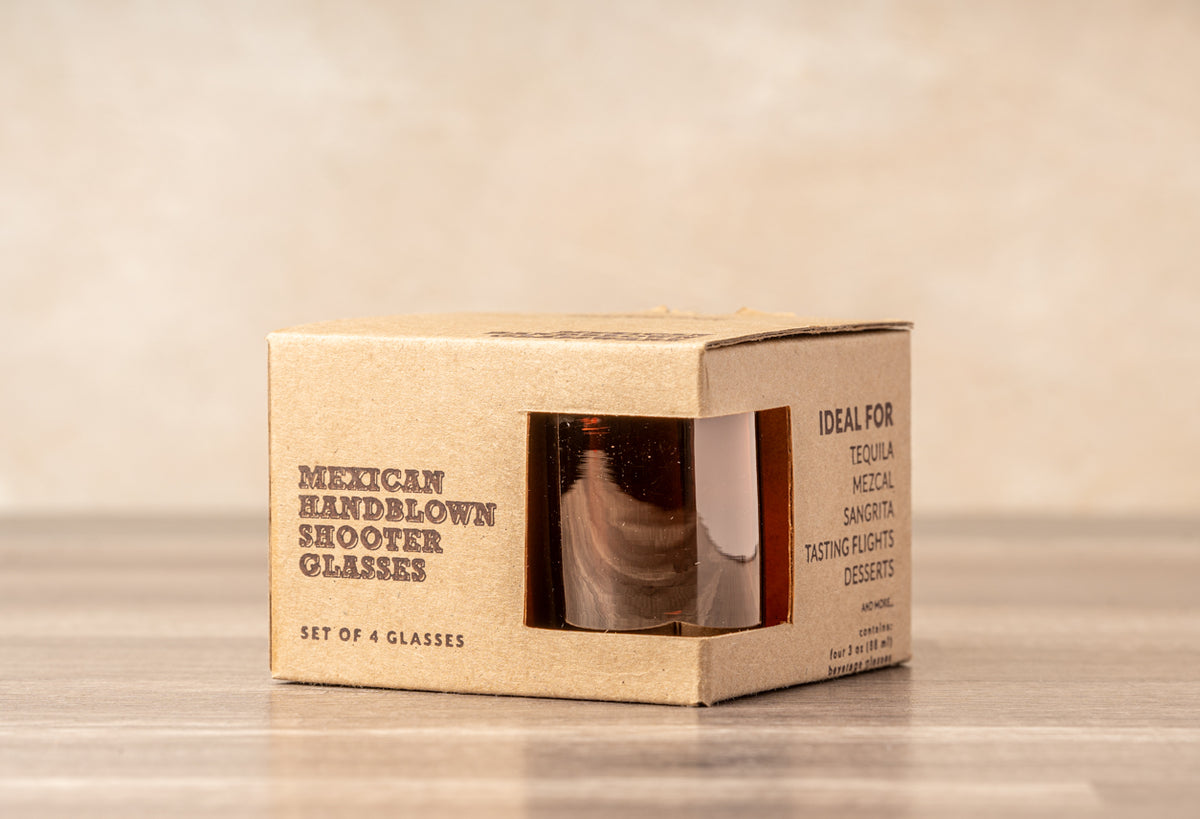 Kraft cardboard box containing four small amber-tinted handblown glass shooter glasses with visible through window.