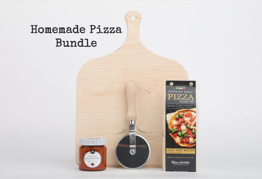 Wooden pizza peel, pizza cutter wheel, jar of sauce, and pizza crust kit box arranged on white background.