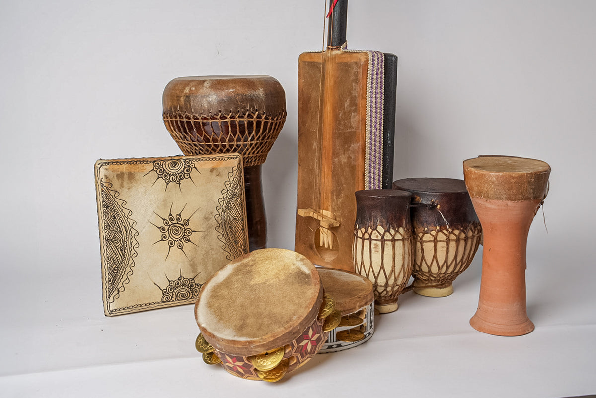 Square-shaped Moroccan drum with geometric sun designs on cream leather surface, displayed among various wooden and clay perc