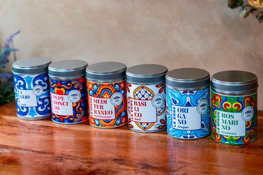 Six decorative metal tins with colorful Italian patterns containing dried herbs and spices.