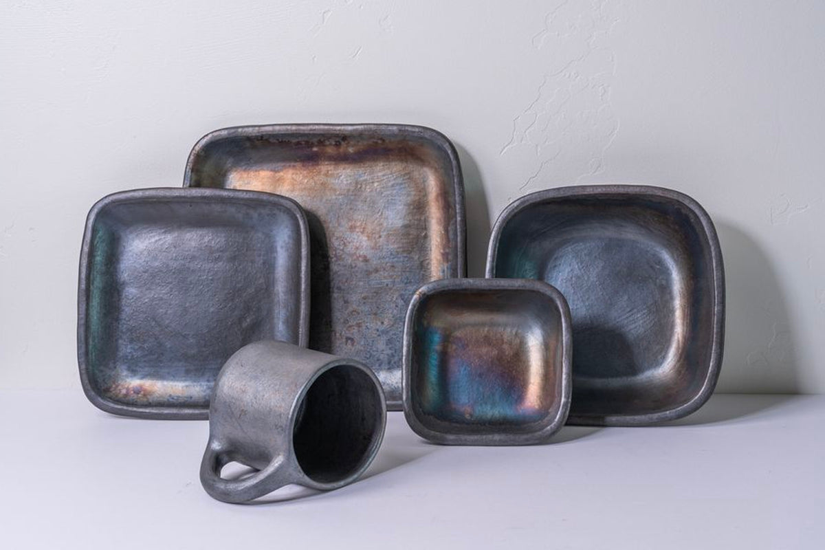 Dark metallic ceramic plates and mug with iridescent glaze finish in various square and rounded shapes.