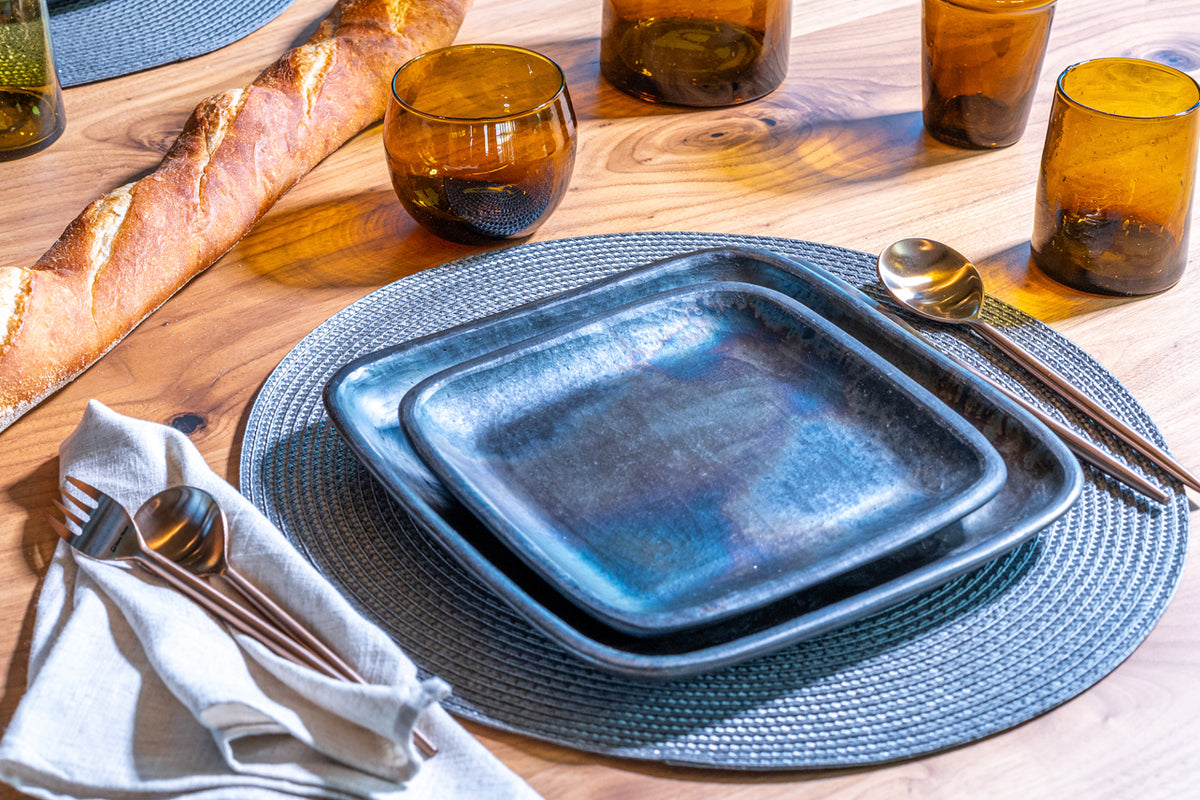 Blue-gray handcrafted pottery dinner plate with textured surface, displayed on matching placemat in table setting.